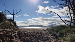 Una playa con cielo despejado, montañas a lo lejos y una persona caminando.