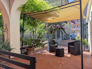 En uteplats med en pergola, sittplatser, krukväxter och utsikt över gatan.