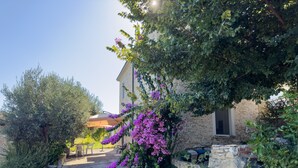 Un edificio de piedra con un jardín que presenta flores moradas y una pérgola.