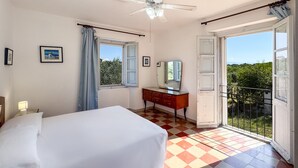Un dormitorio con cama, cómoda, ventilador de techo, ventana con cortinas y balcón con vistas.