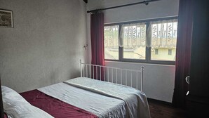 Makuuhuone, jossa on yksi sänky, ikkuna, jossa on verhot, ja näkymä ulos.