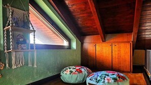 Tunnelmallinen huone, jossa on puupalkit, kalteva katto ja ikkuna, josta on kaunis näkymä. Huoneessa on kaksi säkkituolia ja roikkuva makrame-koriste.