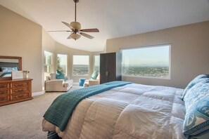 Makuuhuoneessa on suuri sänky, kattotuuletin, lipasto ja suurista ikkunoista avautuva näkymä kaupunkimaisemaan.