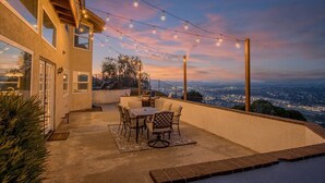 An outdoor patio with a table and chairs, string lights, and a view of a cityscape at dusk. - Exceptional city light views- 5 min to Old Town (Temecula)