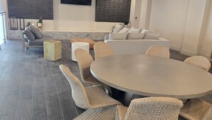 Um espaço interior moderno com uma mesa redonda cercada por cadeiras de vime, um sofá e uma televisão de tela plana fixada em uma parede de tijolos.