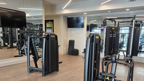 Uma academia com equipamentos de ginástica, um espelho e uma televisão de tela plana.