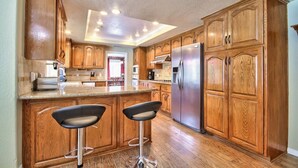 A kitchen with wooden cabinets, a stainless steel refrigerator, and two bar stools. - Rancho Vista Estate on 3 acre, Private grapevines (Temecula)