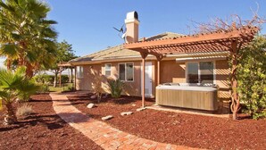 Una casa de un piso con un patio, un jacuzzi y una pérgola.