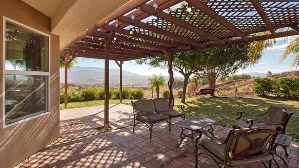 Un patio techado con mobiliario exterior, una pérgola y vistas del paisaje.