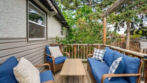 Eine überdachte Veranda mit Korbmöbeln, einem Holztisch und Blick auf einen Garten und Bäume.