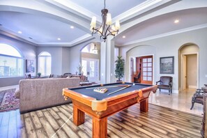 Un salon spacieux avec une table de billard, un canapé et un lustre.