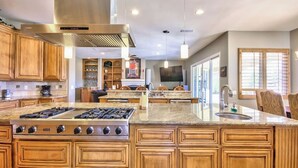 Une cuisine spacieuse dotée de meubles en bois, d’un grand îlot central avec une plaque de cuisson intégrée et d’un coin repas avec un téléviseur placé au-dessus du comptoir.