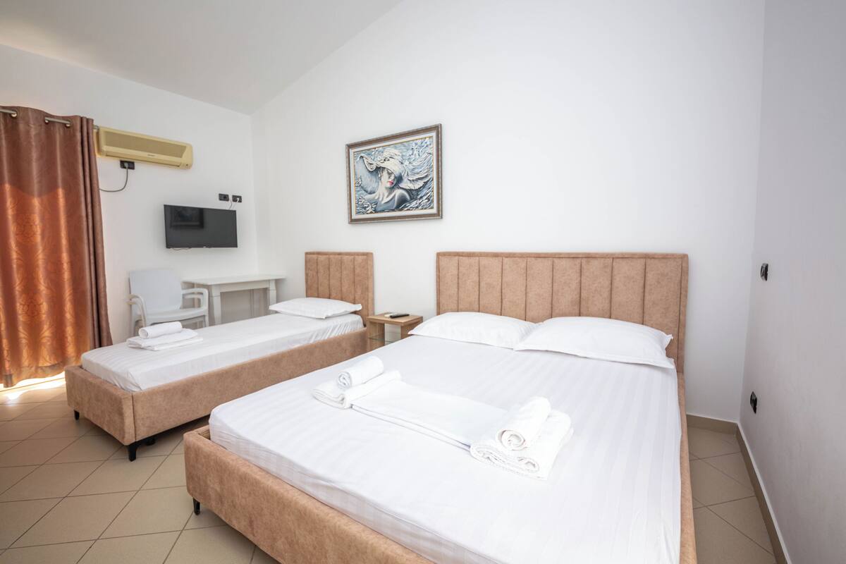 A hotel room with two beds, a desk, a chair, a TV, and a painting on the wall.