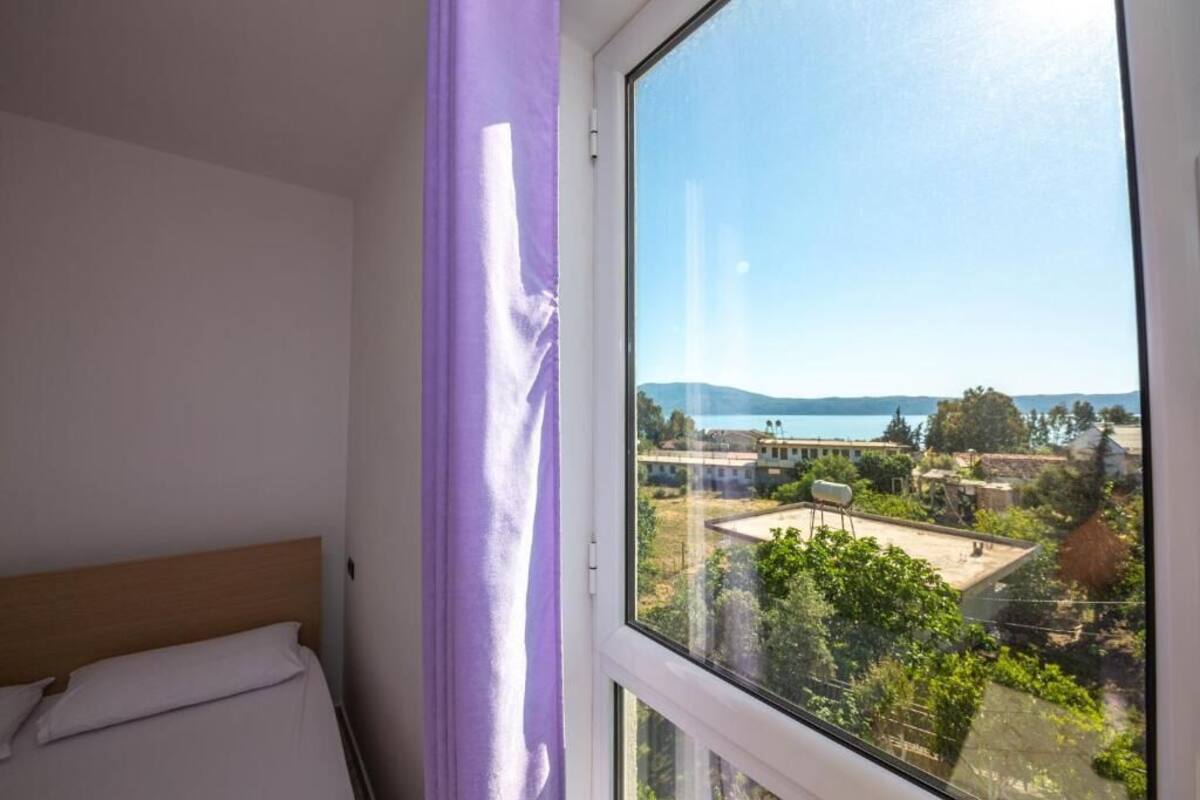 A bedroom with a large window overlooking a residential area and a body of water.