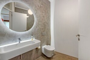 A bathroom with a white sink, a toilet, a round mirror, and a light fixture. - Spacious and Bright Apartment II (Porto)