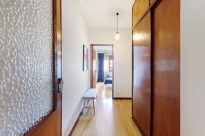 A hallway with a bench, wooden doors, and a hanging light fixture. - Spacious and Bright City Apartment – No Elevator (Porto)
