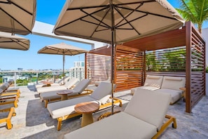A rooftop lounge area with sun loungers, umbrellas, and a view of the cityscape. - Domus Accessible 1BR Condo with Balcony (Miami)