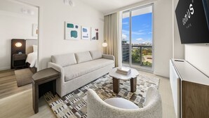 Habitación de hotel moderna con sofá, sillón, mesa de centro y un ventanal con vistas a la ciudad.