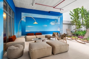 A modern outdoor seating area with sofas, chairs, and a table, featuring a blue sky mural and a tree. - Elegant 2BR Condo at Domus with Hot Tub & Gym (Miami)