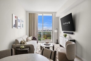 A modern hotel room with a sofa, a dining table, a flat-screen TV, and a view of the city through a large window. - Domus 1BR Retreat. Short Drive to Little Havana (Miami)