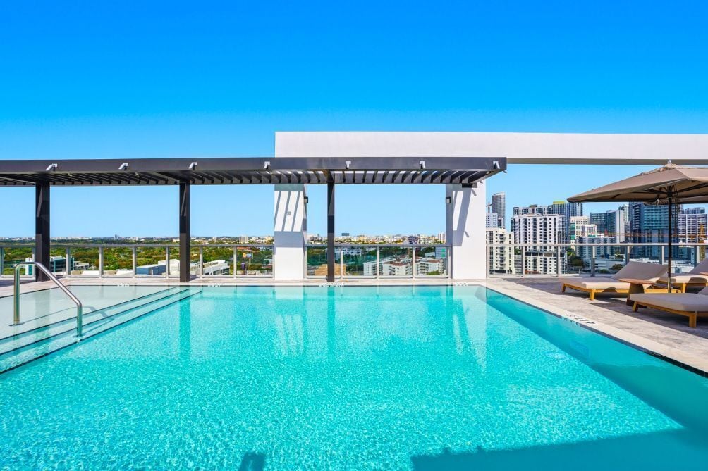 A rooftop pool with a city view, a pergola, and lounge chairs.