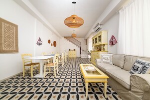 Un salon avec un sol à motifs, un canapé, une table basse, une table à manger avec des chaises, un escalier et un luminaire suspendu.