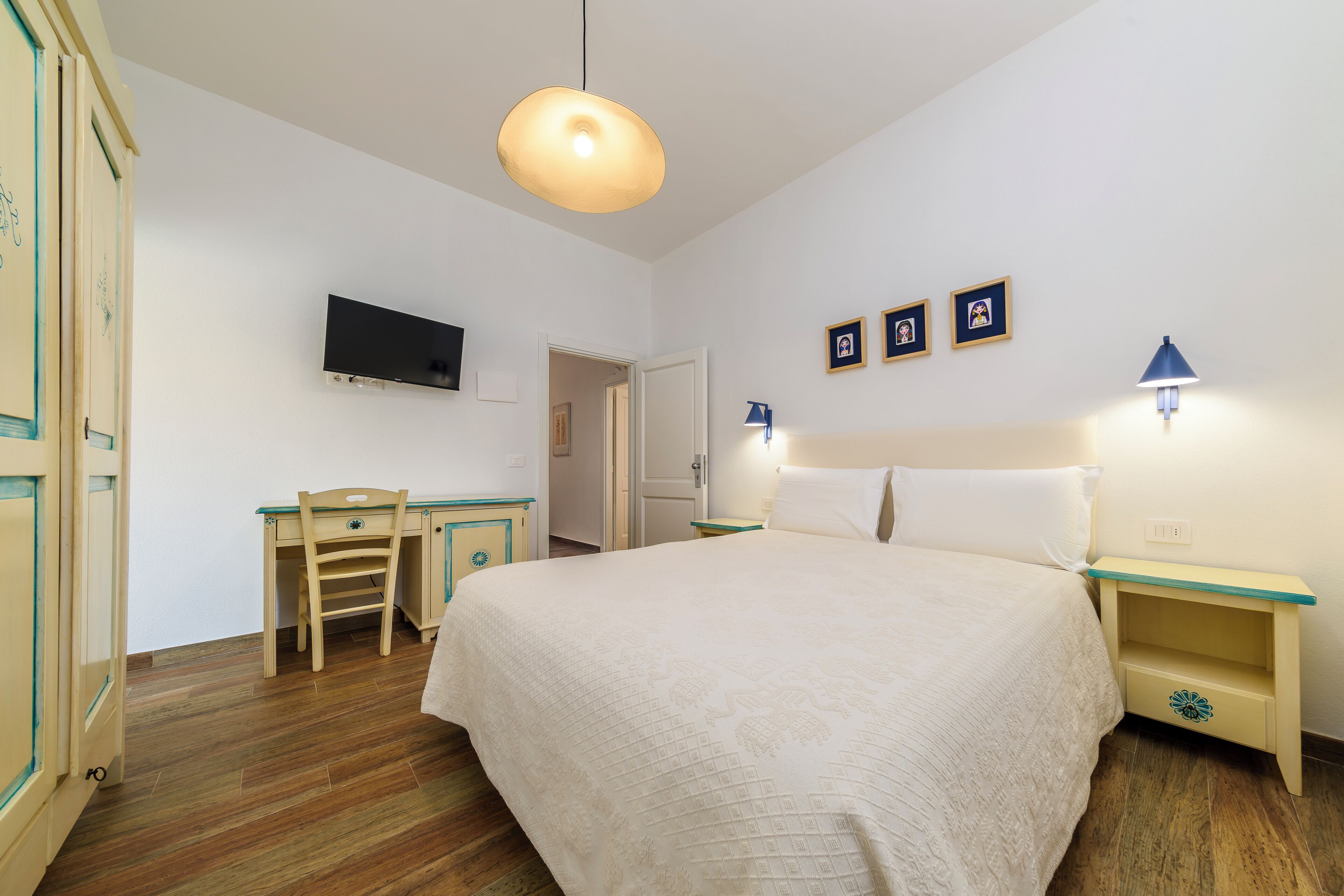 A bedroom with a bed, a desk, a chair, a television, and wall-mounted lights.