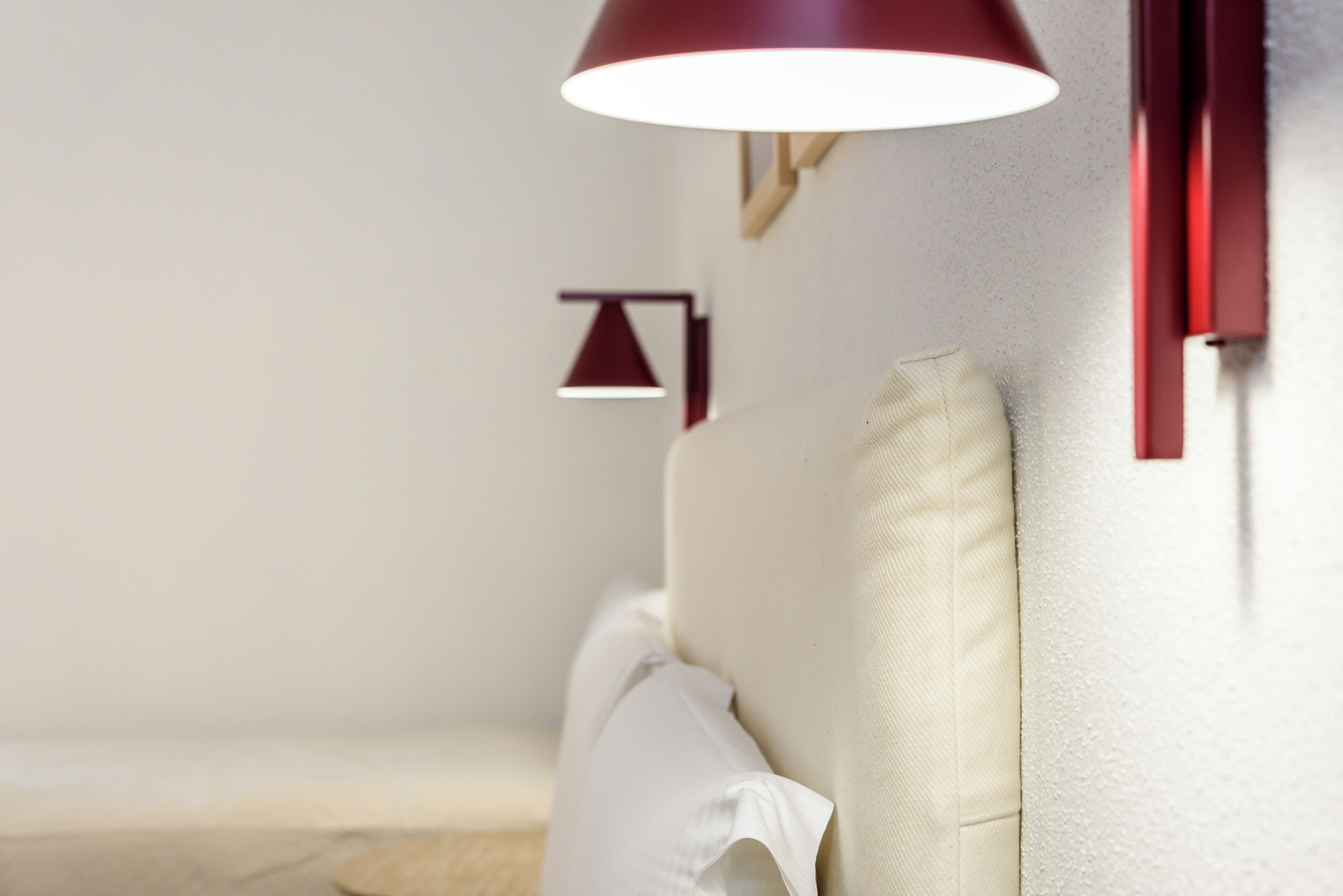 A room with a white sofa, a red wall-mounted lamp, and a small white table.