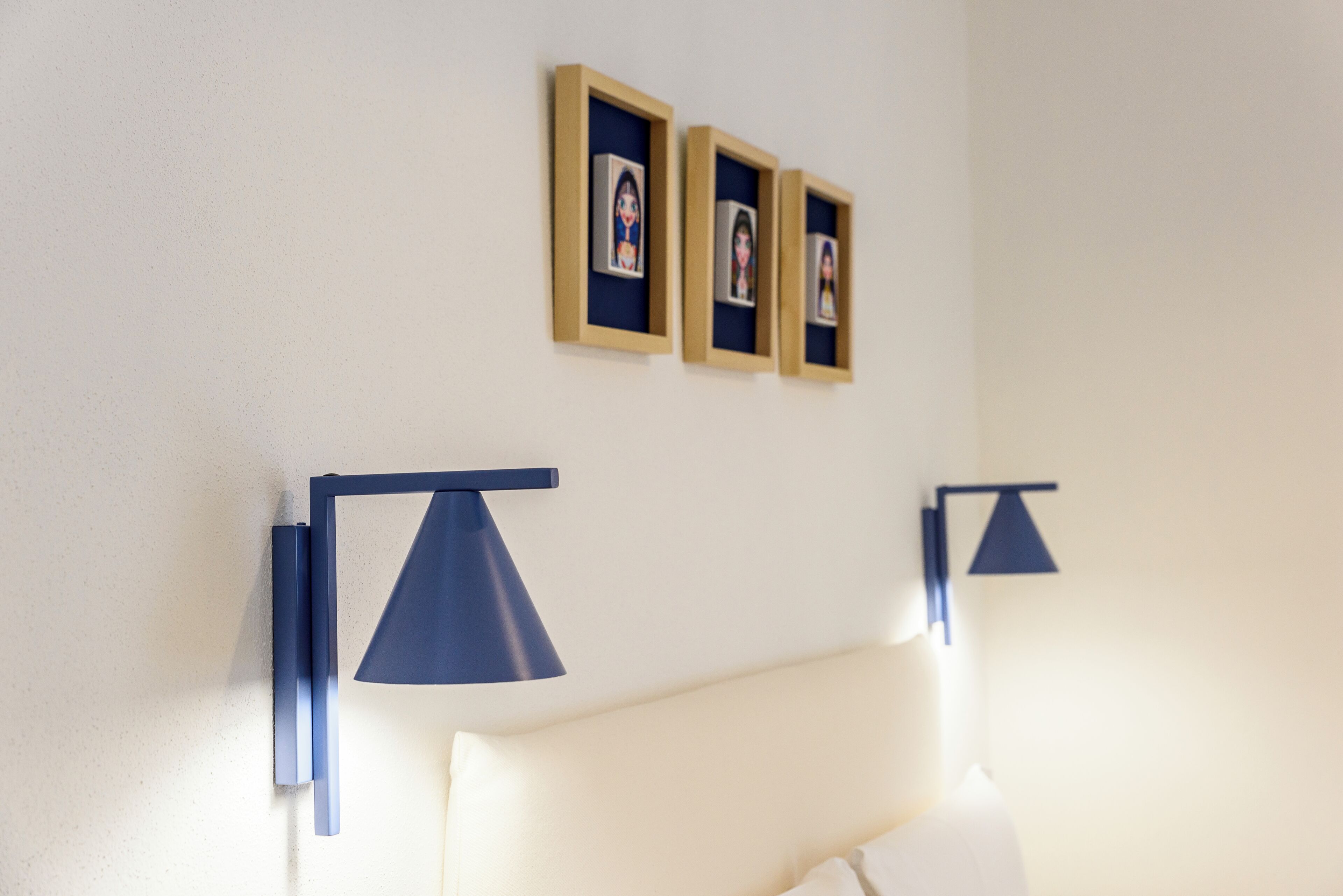 A room with a bed, two wall-mounted lamps, and three framed photos on the wall.