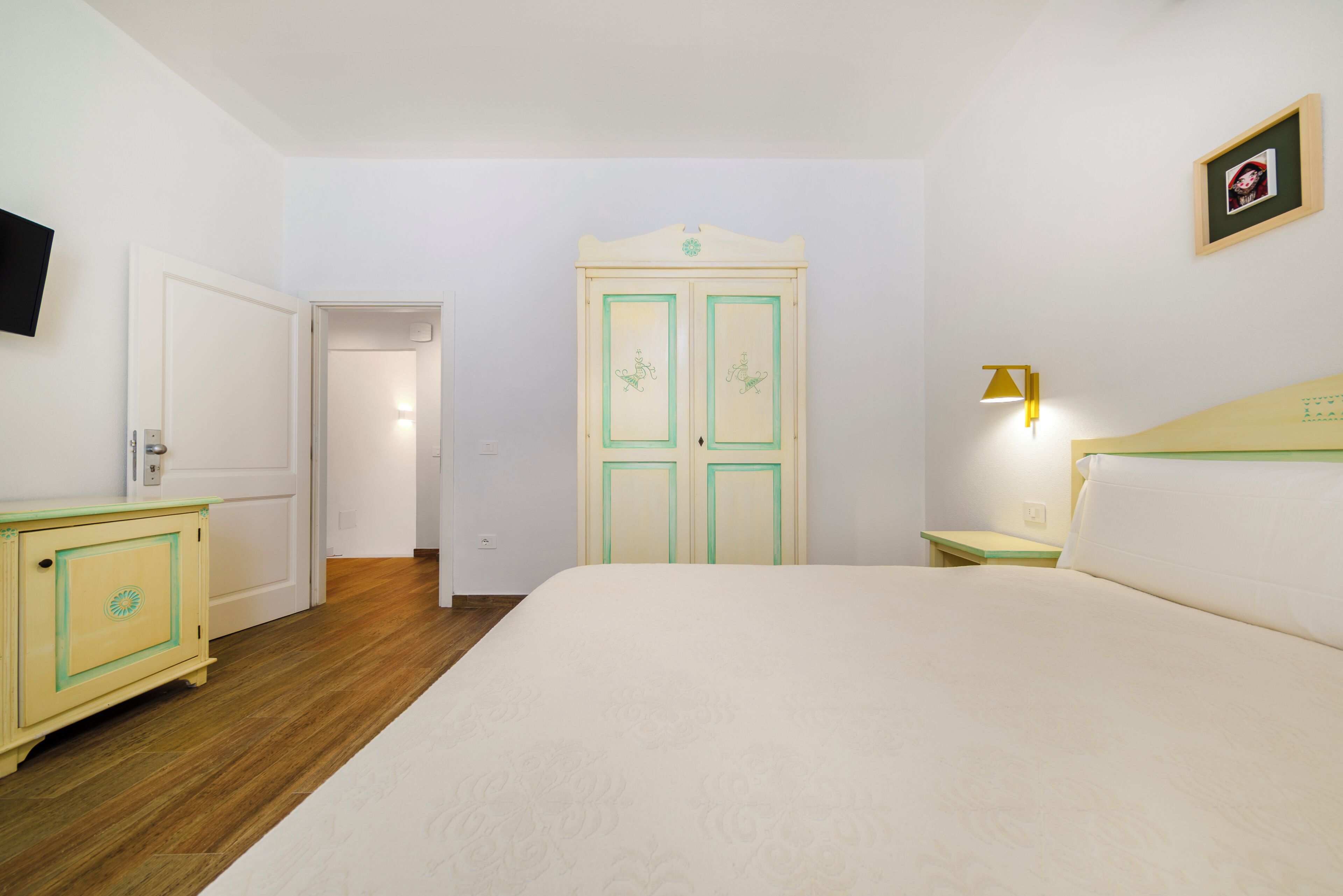 Habitación de hotel con cama, armario, mesita de noche, lámpara y televisor.