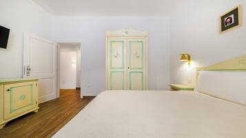 Habitación de hotel con cama, armario, mesita de noche, lámpara y televisor.