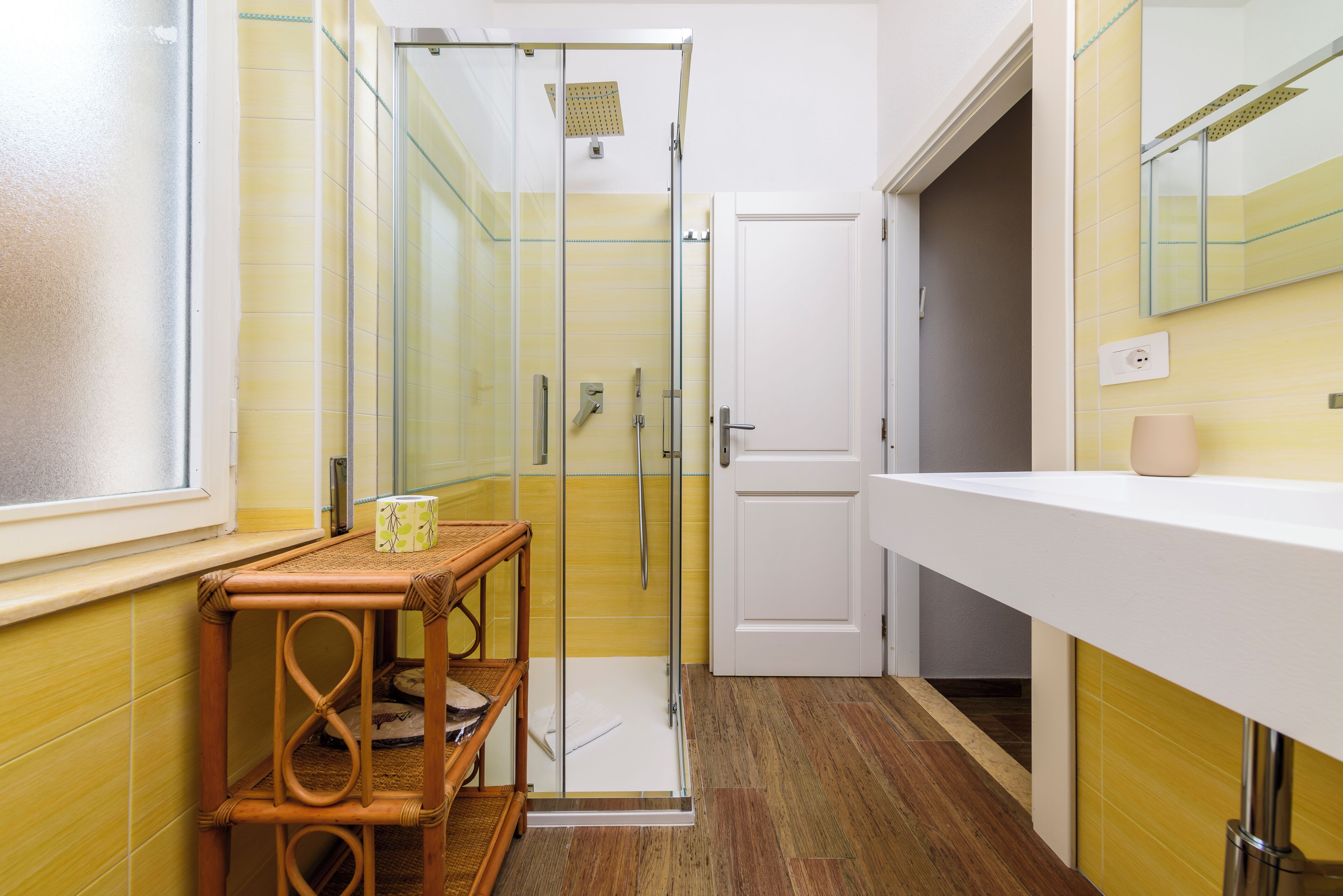Une salle de bain avec une douche à parois de verre, une porte blanche et une table en bois sur laquelle est posée une serviette.