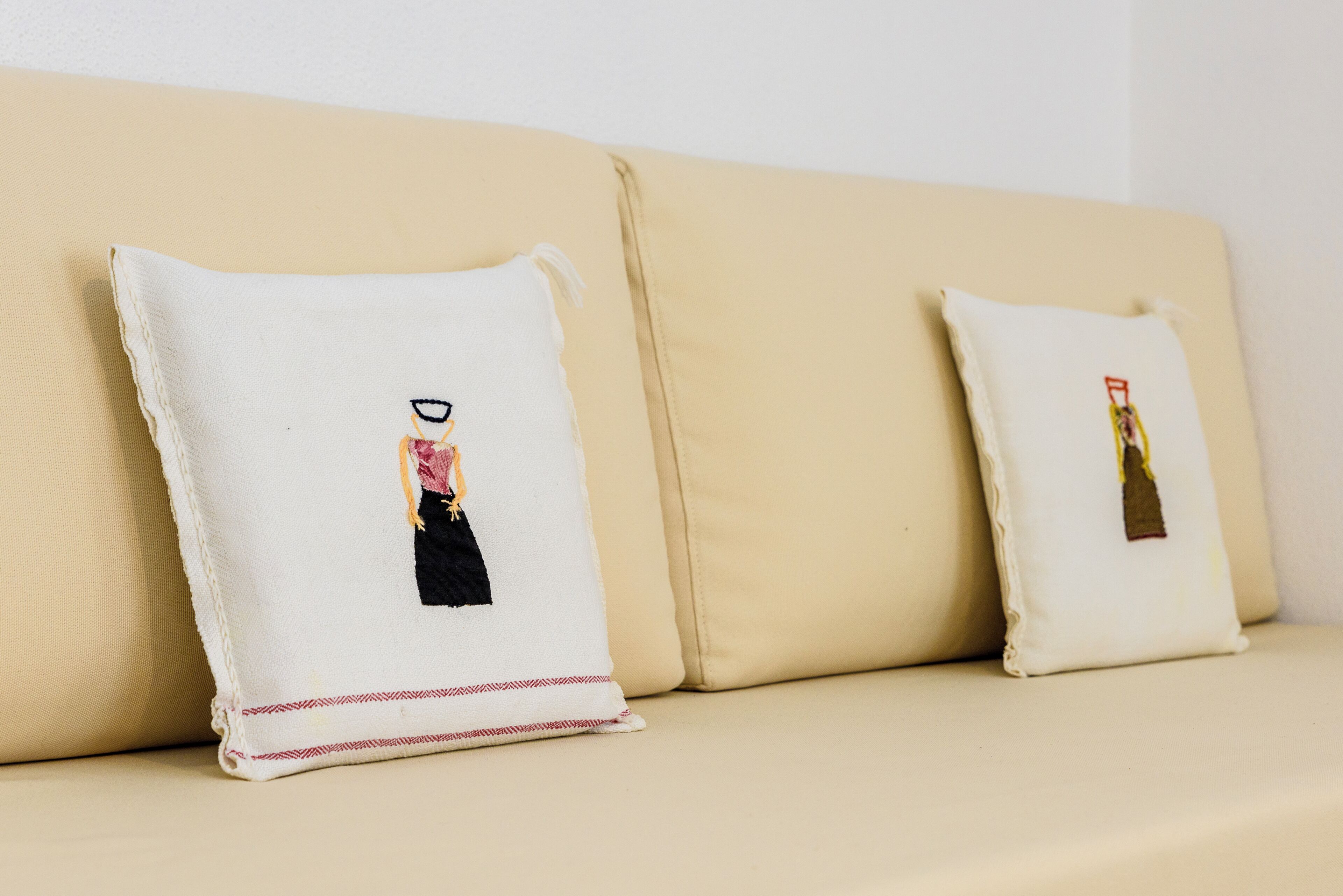 Un sofá beige con dos almohadones, cada uno con un pequeño diseño bordado.