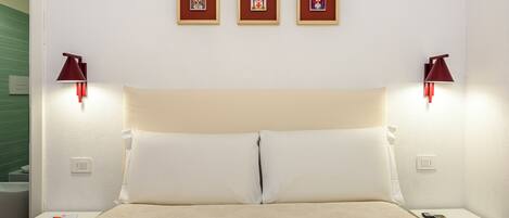 A hotel room with a bed, two bedside tables, a nightstand, a wall-mounted lamp, and three framed pictures on the wall.