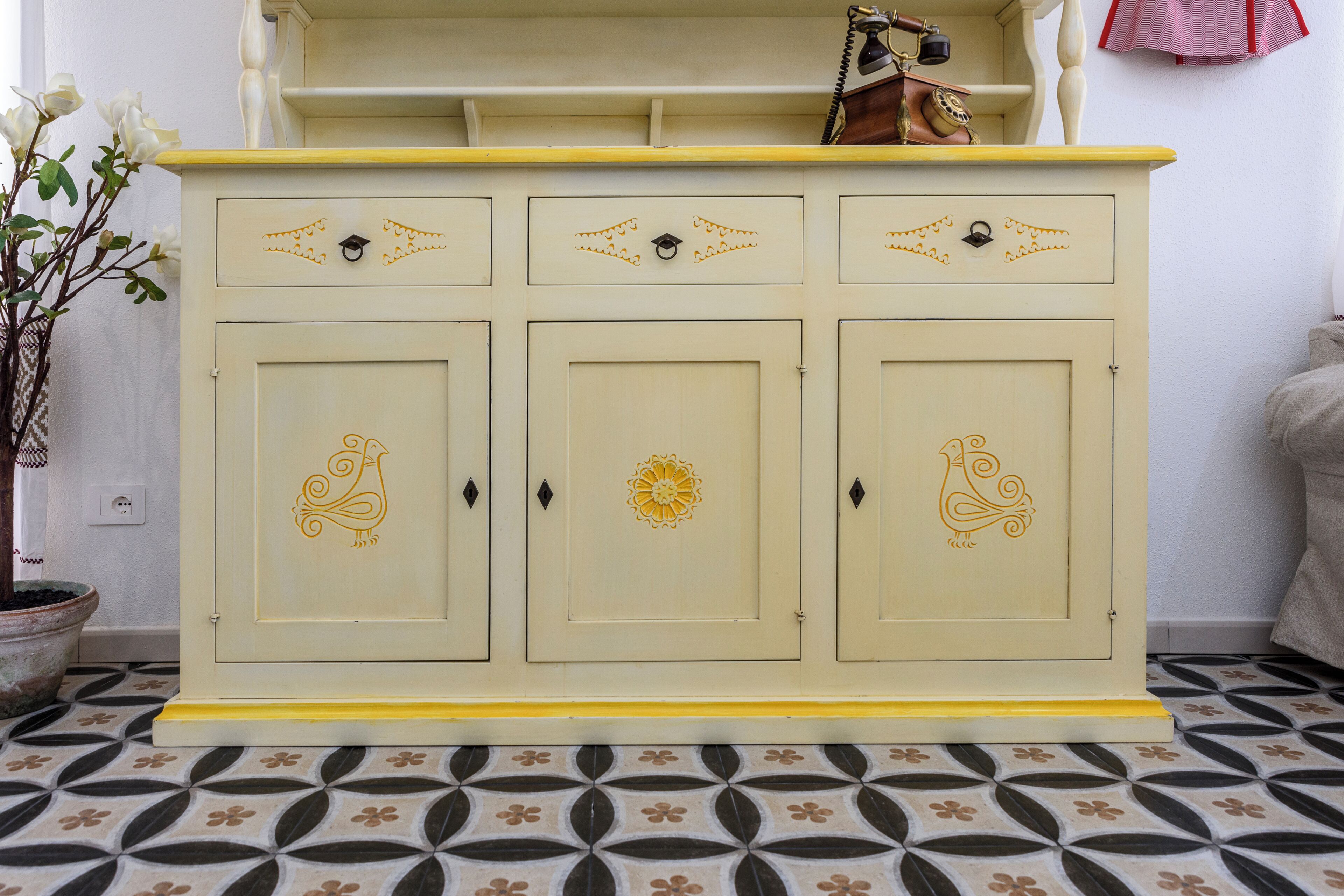 A cream-colored cabinet with decorative patterns on the doors and a yellow top shelf.