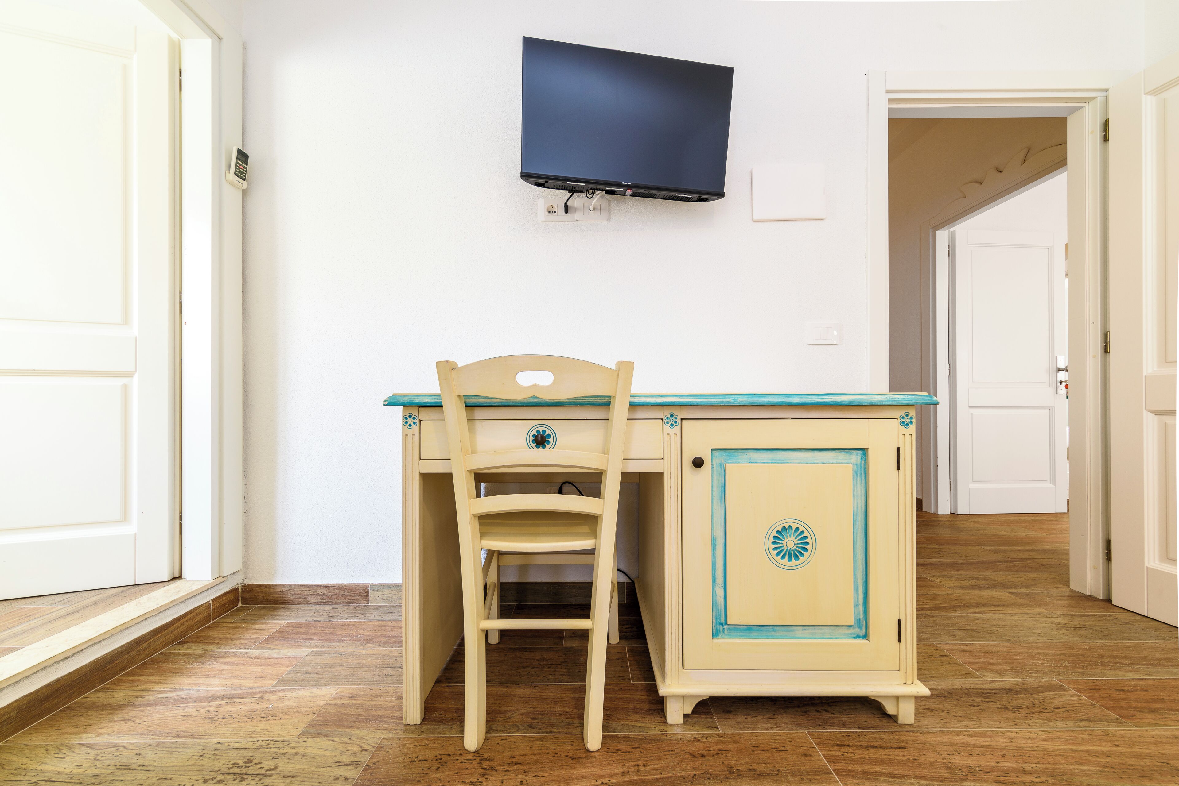 A room with a desk, chair, TV mounted on the wall, and a door.
