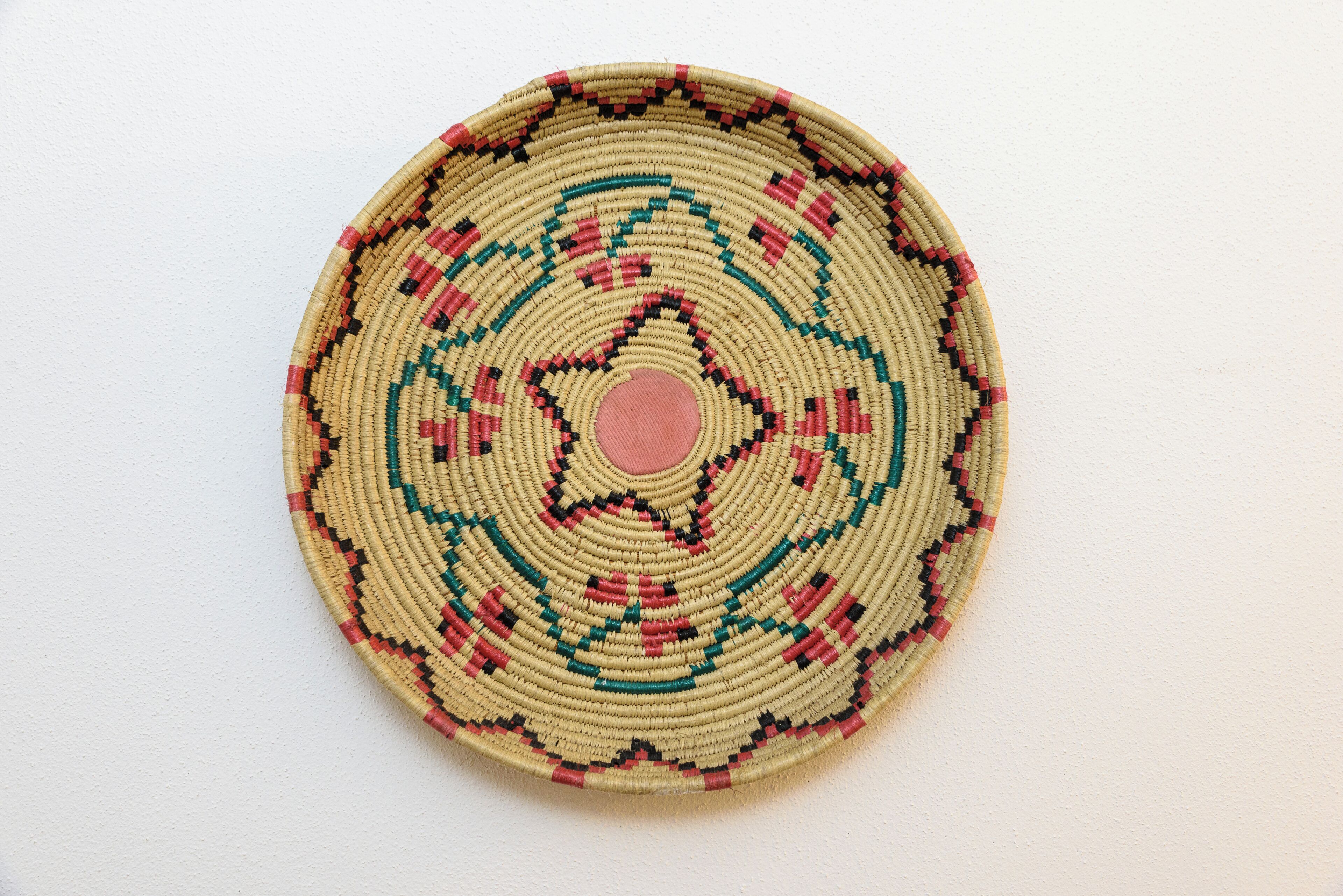 A circular woven object with a central pink dot and a geometric pattern.