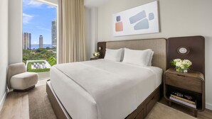 A hotel room with a large bed, a view of the cityscape, a side table with a vase of flowers, and a window with curtains. - Modern 1BR Retreat in Miami – Bay Views (Miami)