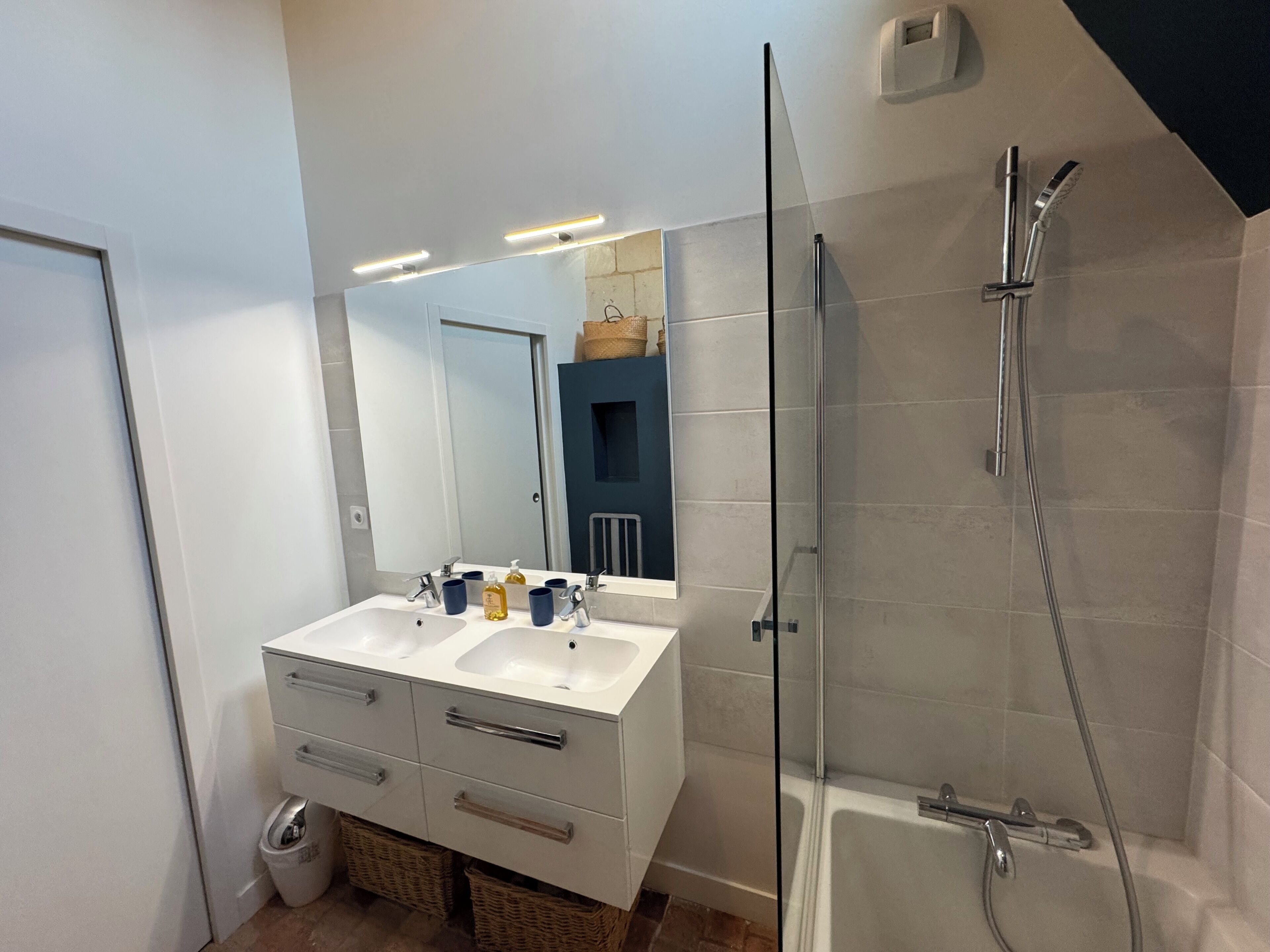 A modern bathroom with two sinks, a large mirror, and a glass-enclosed shower.