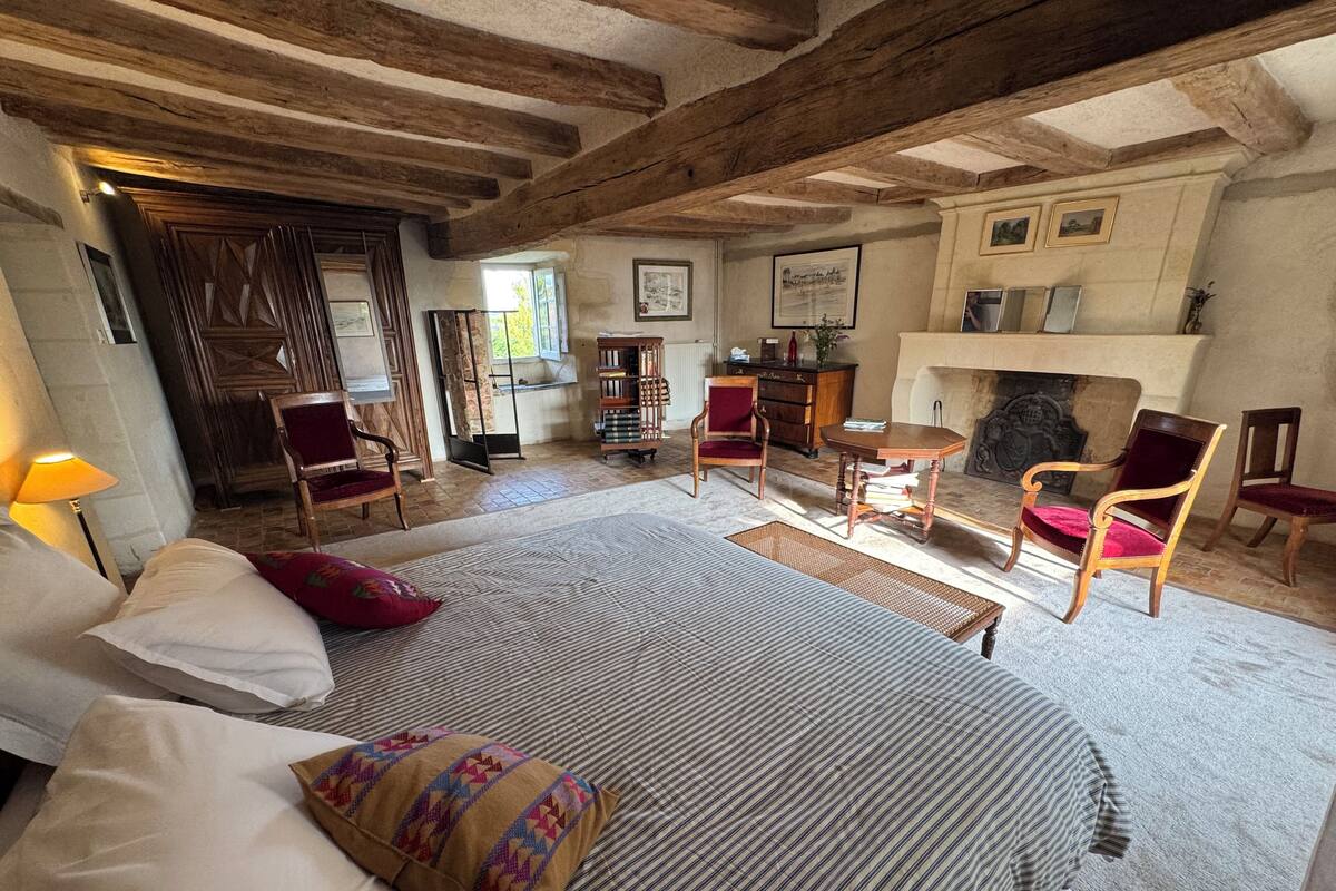 Une chambre spacieuse avec un grand lit, plusieurs chaises, une petite table et une cheminée.