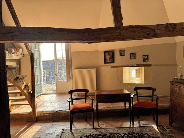 A rustic room with exposed wooden beams, a wooden staircase, a dining table with chairs, and a radiator. - Le Clos Marie 49 (Mazé-Milon)