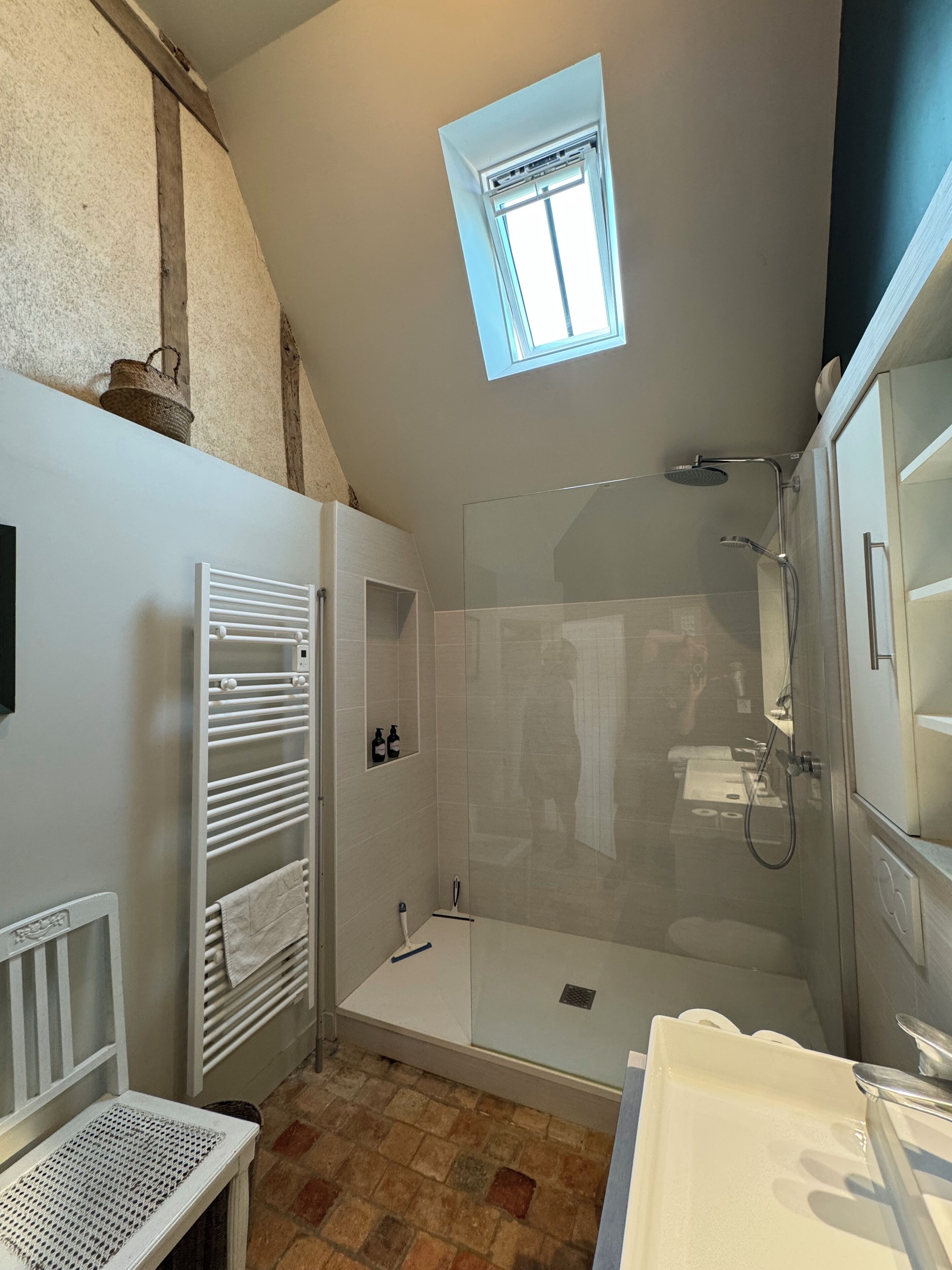 Casa de banho moderna com chuveiro de vidro, uma pequena clarabóia e radiador branco.