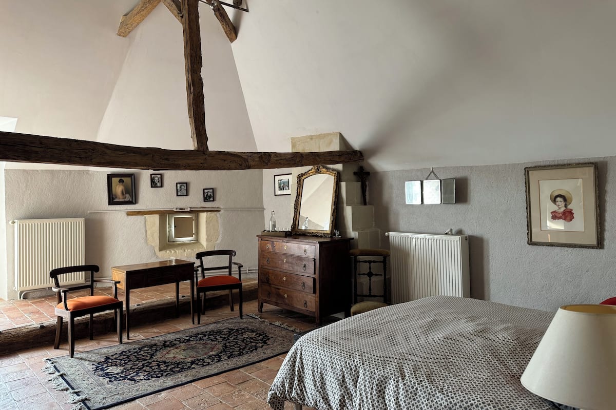 Une chambre avec un plafond en pente, des poutres en bois, un lit, une commode, une chaise, une table et un tapis.