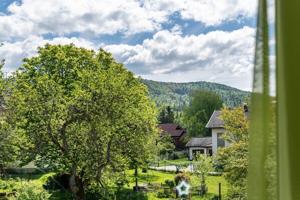 A rural landscape with a large tree, houses, and a hilly background.