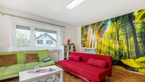 A living room with a green sofa, a red sofa, a white coffee table, and a bookshelf with toys.