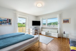 Ein Schlafzimmer mit Bett, Fernseher, Schreibtisch und Blick ins Freie.