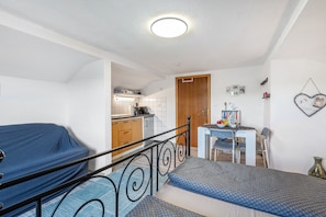 Un dormitorio con una cama, una mesita y una kitchenette al fondo.