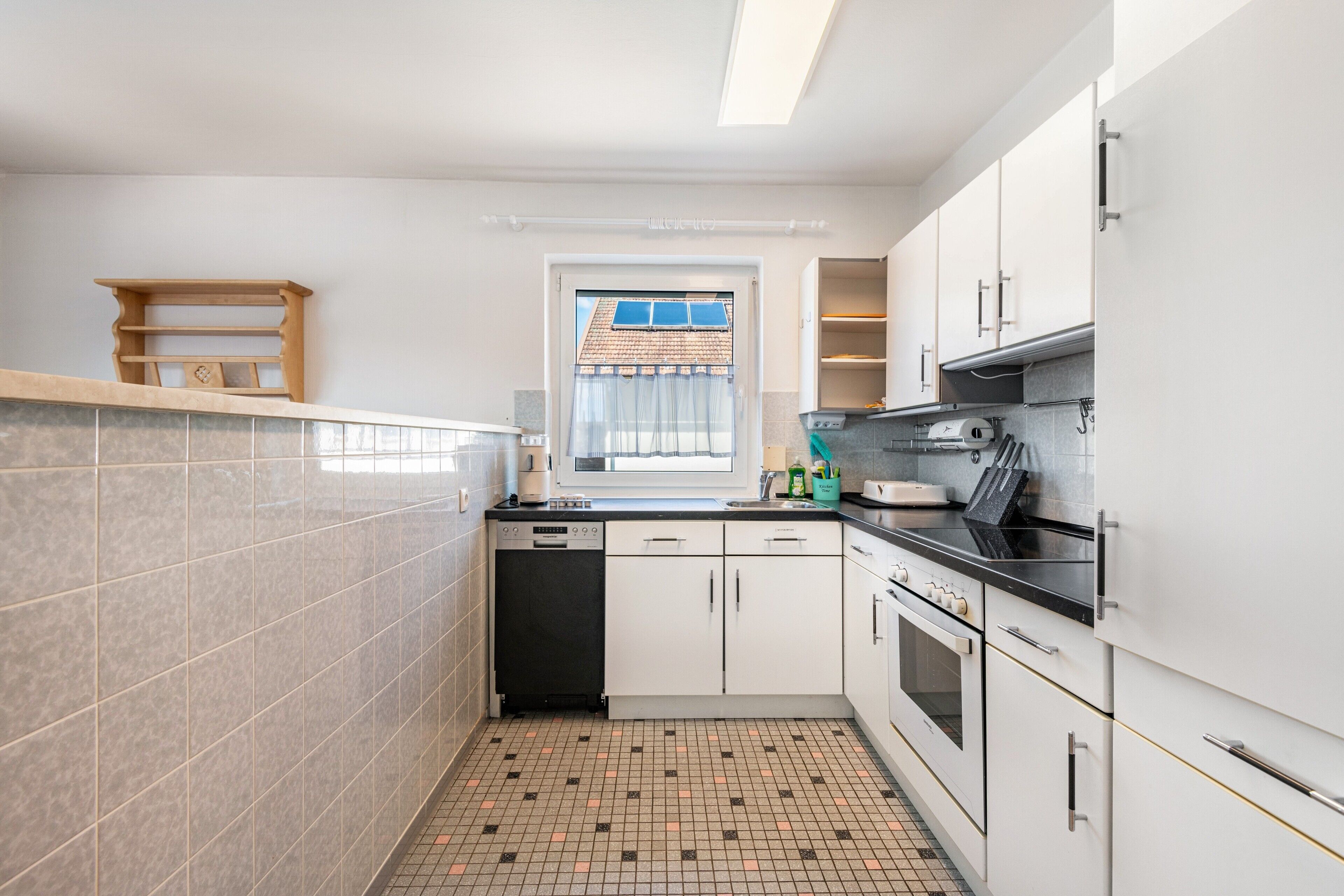 A modern kitchen with white cabinets, a black countertop, and a tiled floor.