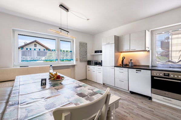 Una cocina moderna con muebles blancos, una mesa de comedor con mantel estampado y vistas a una casa a través de la ventana.