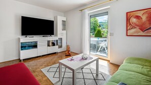 Una sala de estar moderna con una televisión de pantalla plana, muebles blancos, un comedor con mesa y sillas, y un sofá verde.